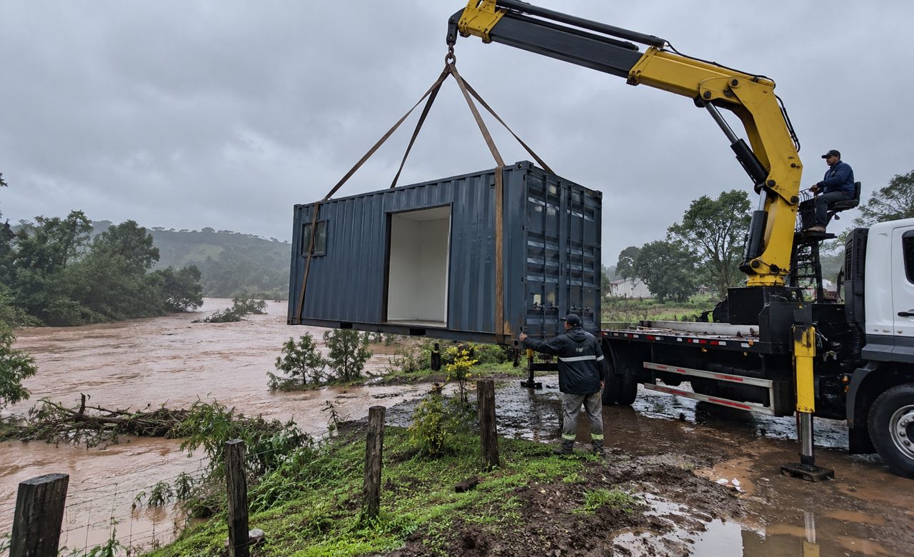 Casa em container sendo transportada por caminhão munck para local seguro durante enchente no Rio Grande do Sul